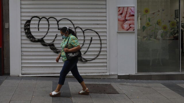 Una mujer pasa por delante de una tienda cerrada durante el confinamiento