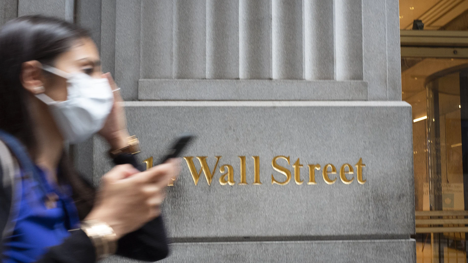 Una mujer con mascarilla pasea por Wall Street, donde tiene su sede la bolsa de Nueva York