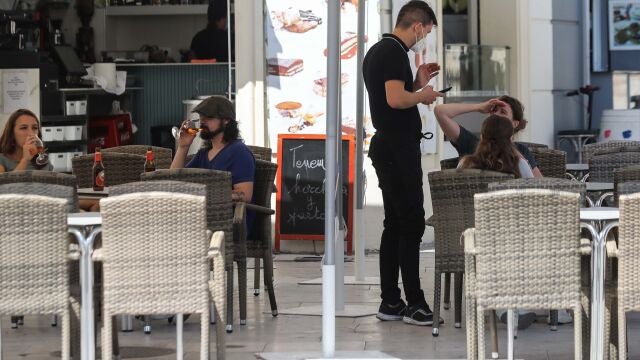 En la imagen, un camarero atiende a unos clientes en la terraza de un bar