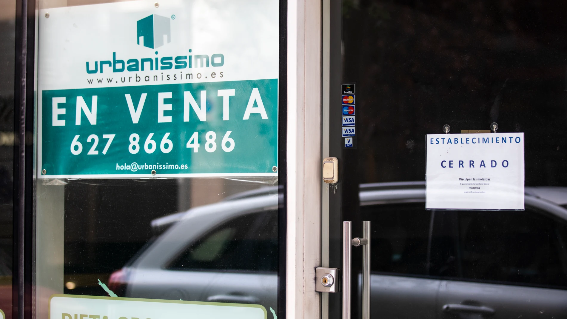 Imagen de un negocio en el que se lee un cartel de establecimiento cerrado, junto a un cartel de una inmobiliaria que anuncia la venta del local