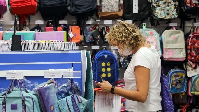 Una mujer, preparada con una lista de material escolar, consulta el precio, en una papelería, de una mochila infanti