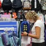 Una mujer, preparada con una lista de material escolar, consulta el precio, en una papelería, de una mochila infanti