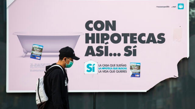 Un hombre con mascarilla pasa por delante del anuncio de una hipoteca en un banco
