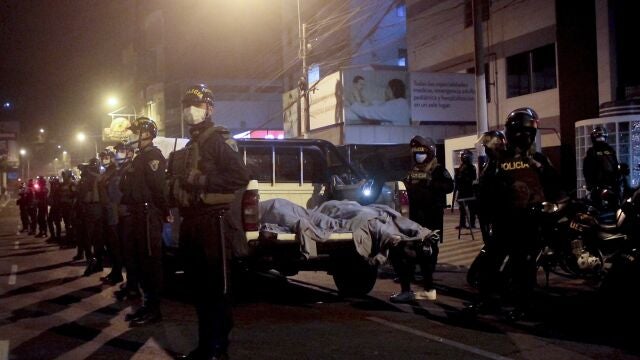 Police officers stand guard near two bodies outside of a disco in Lima, Peru, Sunday, Aug. 23, 2020. Officials said over a dozen people died in a stampede at a disco in Peru after a police raid to enforce the country's lockdown during the coronavirus pandemic. (AP Photo/Diego Vertiz)