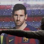 Vista de la estatua dedicada a Johan Cruyff en el Camp Nou, con un cartel publicitario de Leo Messi detrás.