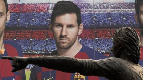Vista de la estatua dedicada a Johan Cruyff en el Camp Nou, con un cartel publicitario de Leo Messi detrás.