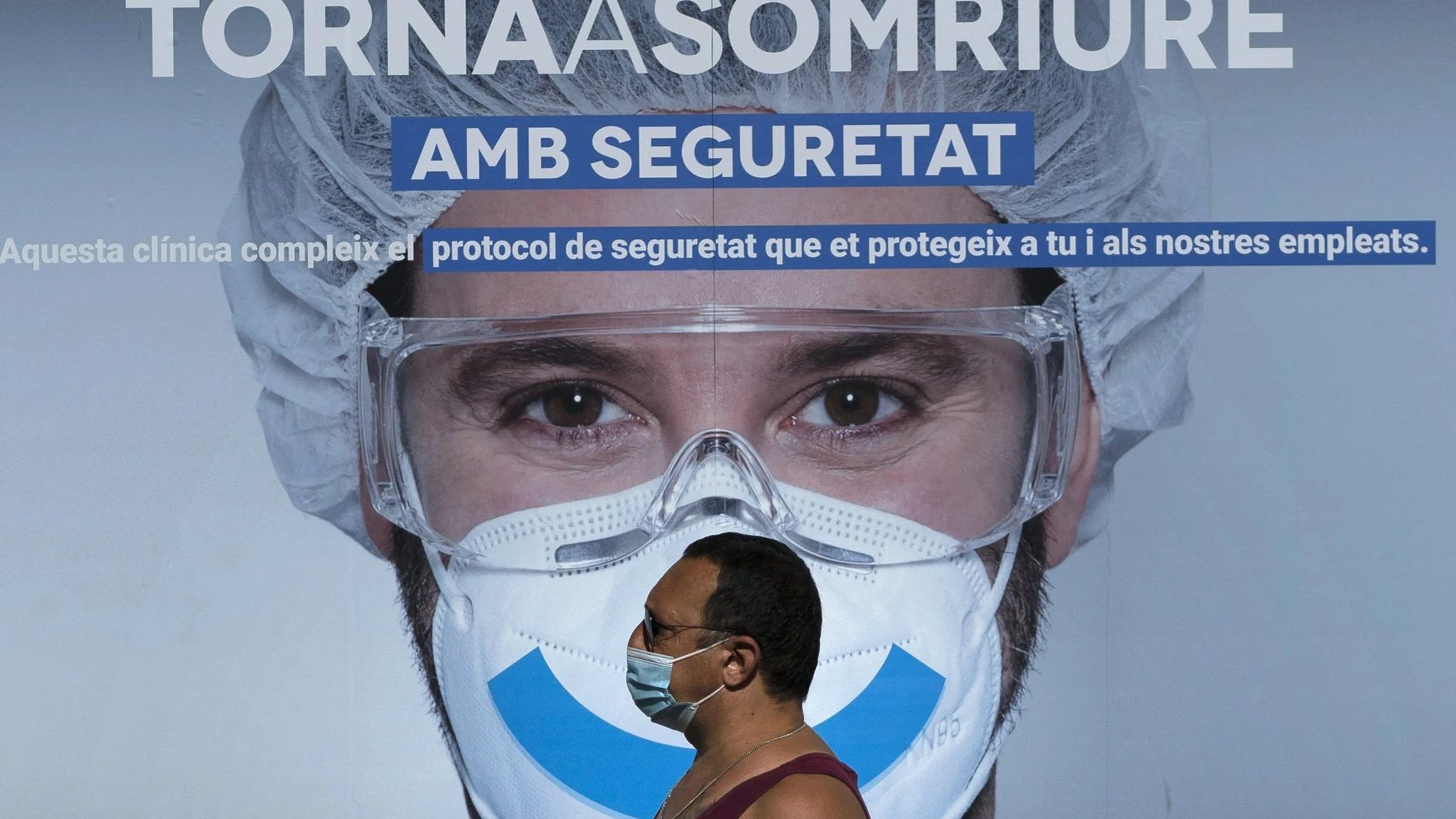 A man wearing face mask walks past an advertising of a private clinic in Barcelona, Spain on Monday Aug. 31, 2020. Spain, with nearly 440,000 infections of the new virus since February, has become western Europe's hardest hit country by a new surging wave of fresh outbreaks. (AP Photo/Emilio Morenatti)