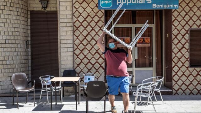 Un hombre recoge las sillas y mesas de la terraza de su negocio en la localidad valenciana de Benigànim (Valencia)