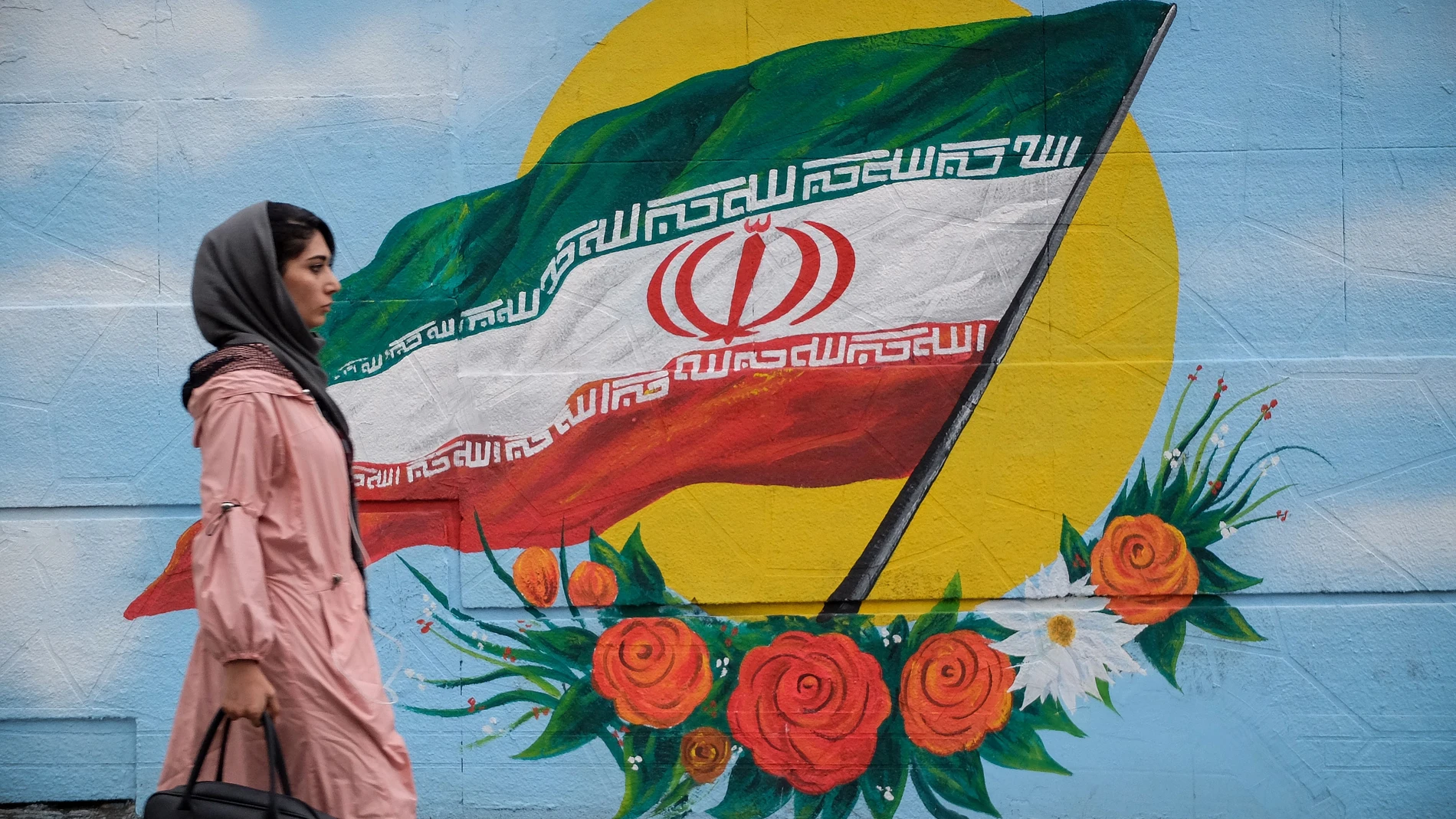 Una mujer camina frente a un mural con la bandera de Irán situado en una de las calles de Teherán.