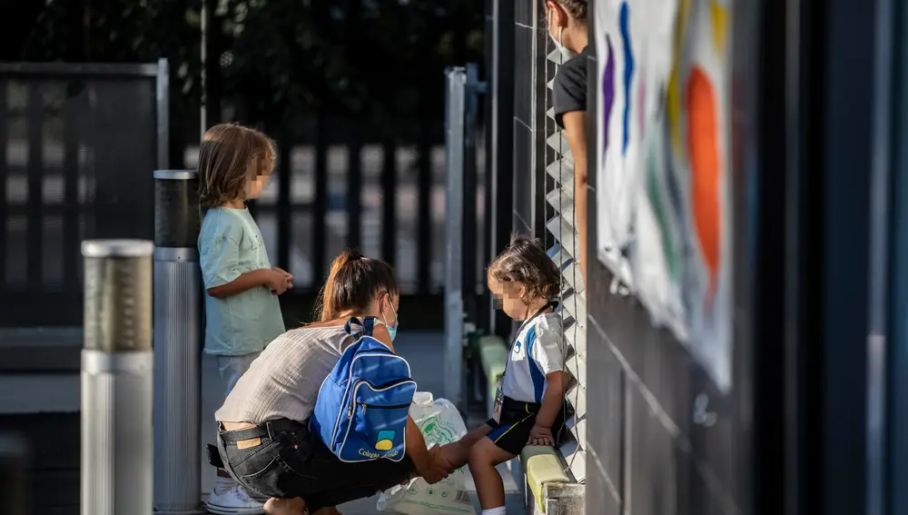 Una madre cambia los zapatos a su hija antes de entrar a la clase en su primer día de colegio