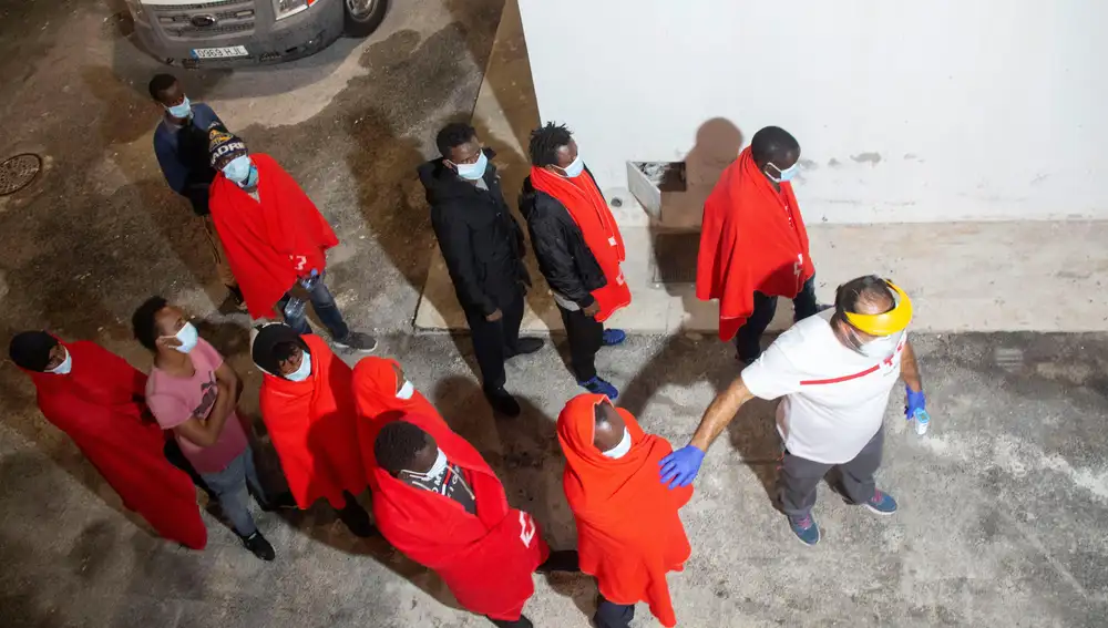 Un trabajador de la Cruz Roja ayuda a los 41 personas de origen subsahariano que han sido rescatados en la madrugada del lunes por efectivos de Salvamento Marítimo trasladados al puerto de Motril