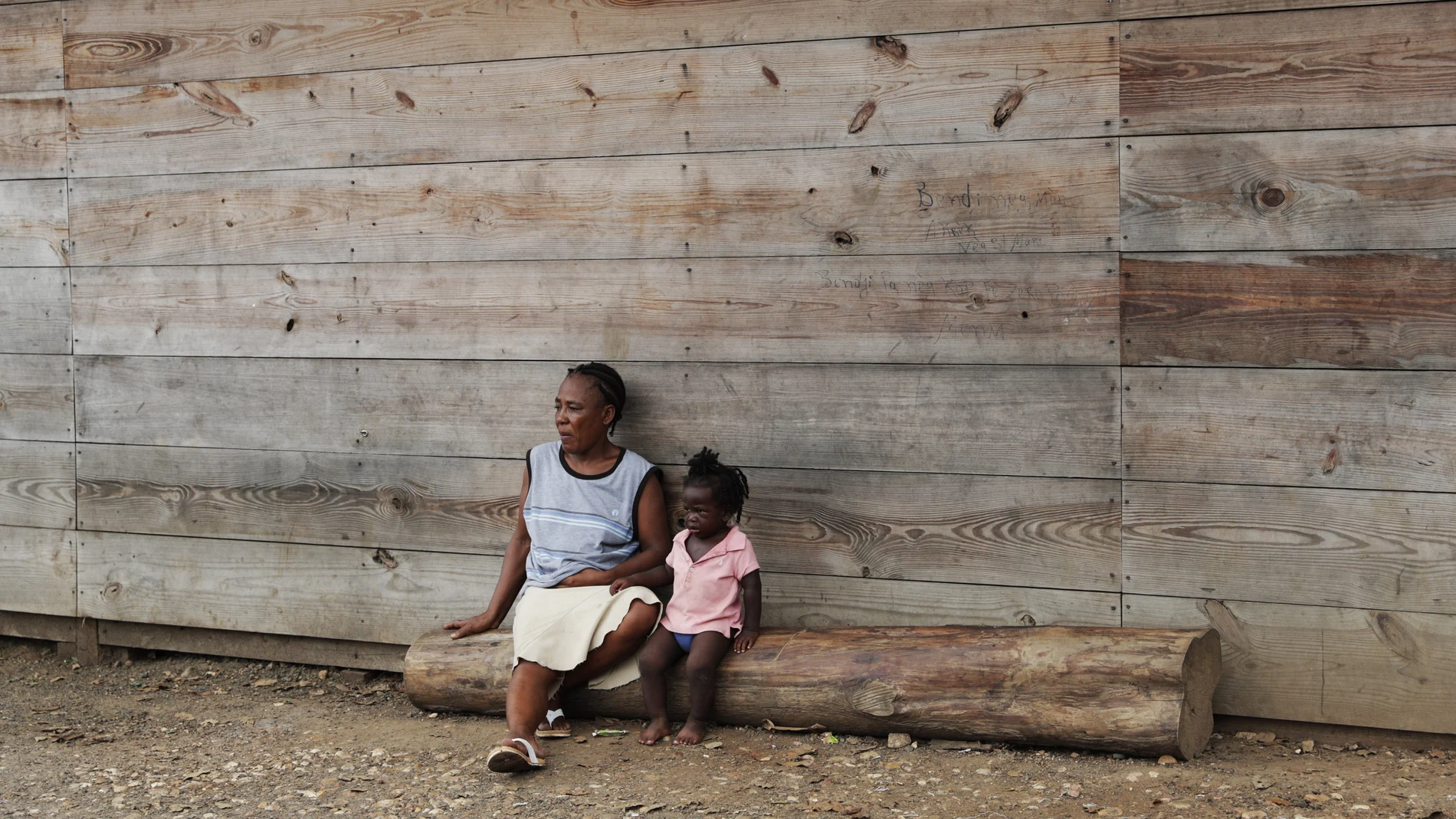 Duperat Laurette sits on a log with a girl at the entrance of a migrant shelter in Lajas Blancas, Darien province, Panama, Saturday, Aug. 29, 2020. The 45-year-old Haitian migrant and her husband emerged from the thick jungle that blankets the Panama-Colombia border here in Darien seven months earlier and have advanced no farther because of the new coronavirus pandemic. (AP Photo/Arnulfo Franco)