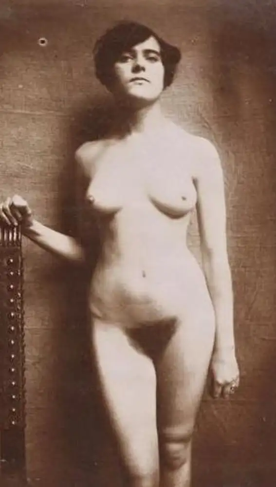 «Mujer desnuda de pie de frente, con la mano derecha apoyada en una silla, sin pie»