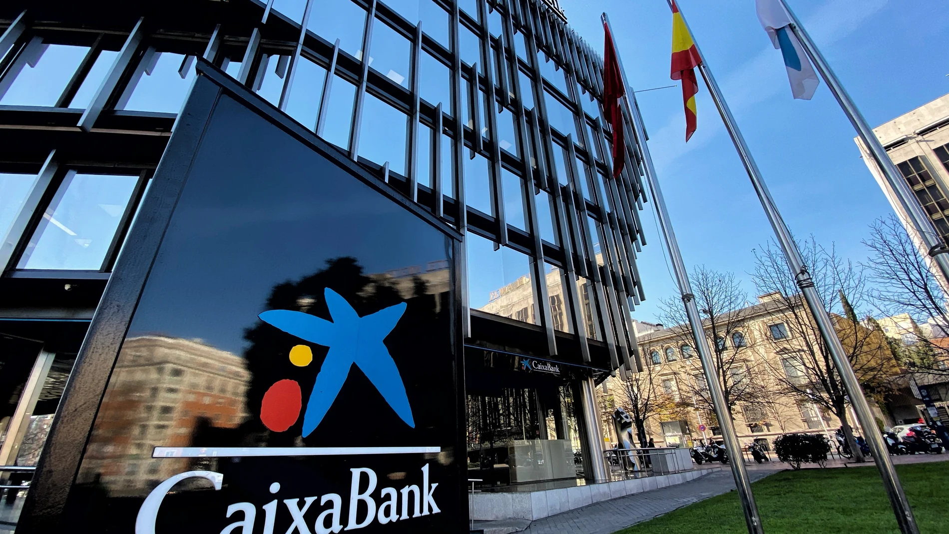 Panel vertical con el logo de Caixa Bank junto a la fachada acristalada de la Sede Central Caixa Bank en Madrid