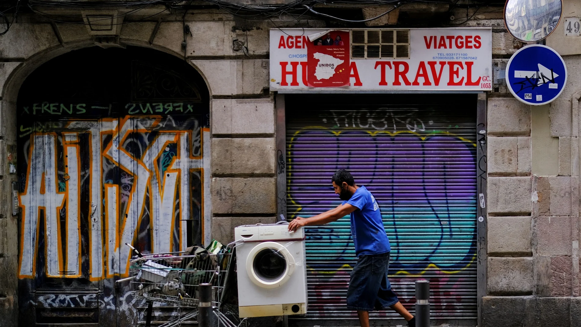 Un hombre empuja un carro con una lavadora en el barrio del Raval, en Barcelona