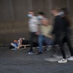 Varias personas con mascarilla pasan junto a un hombre tumbado en la calle en Barcelona