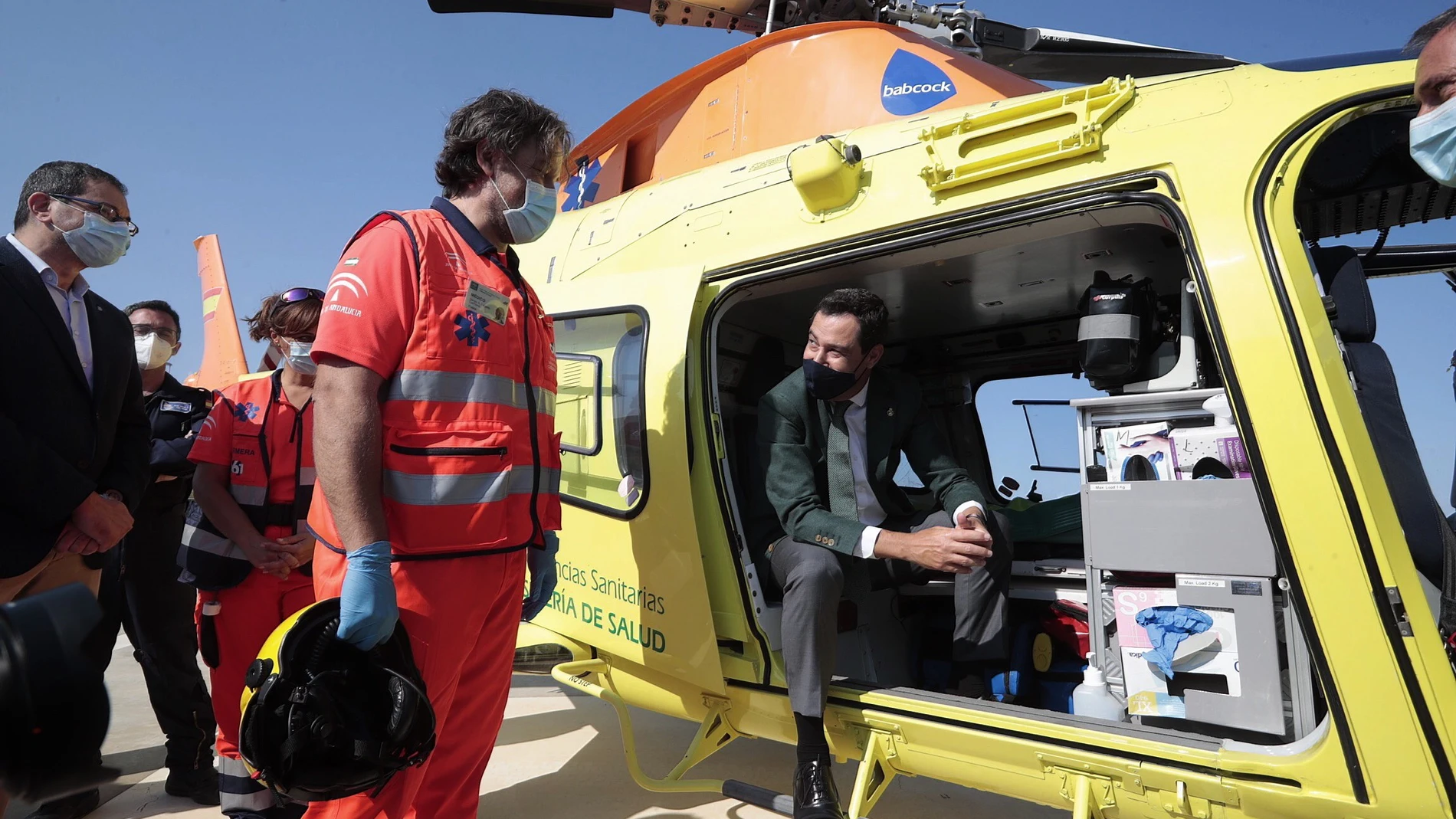 El presidente de la Junta de Andalucía (d), Juanma Moreno, conversa con personal sanitario desde el interior de un helicóptero medicalizado que prestará servicio en el hospital de Jerez de la Frontera (Cádiz), durante el acto de presentación hoy en el helipuerto del centro hospitalario.