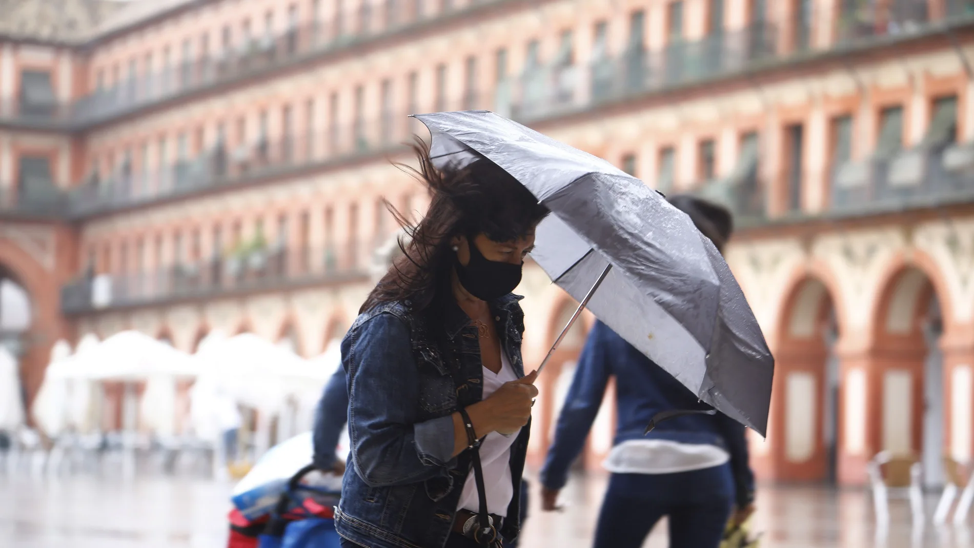 Una joven se resguarda de la lluvia y el viento con un paraguas a su paso por la plaza de la Corredera en Córdoba.