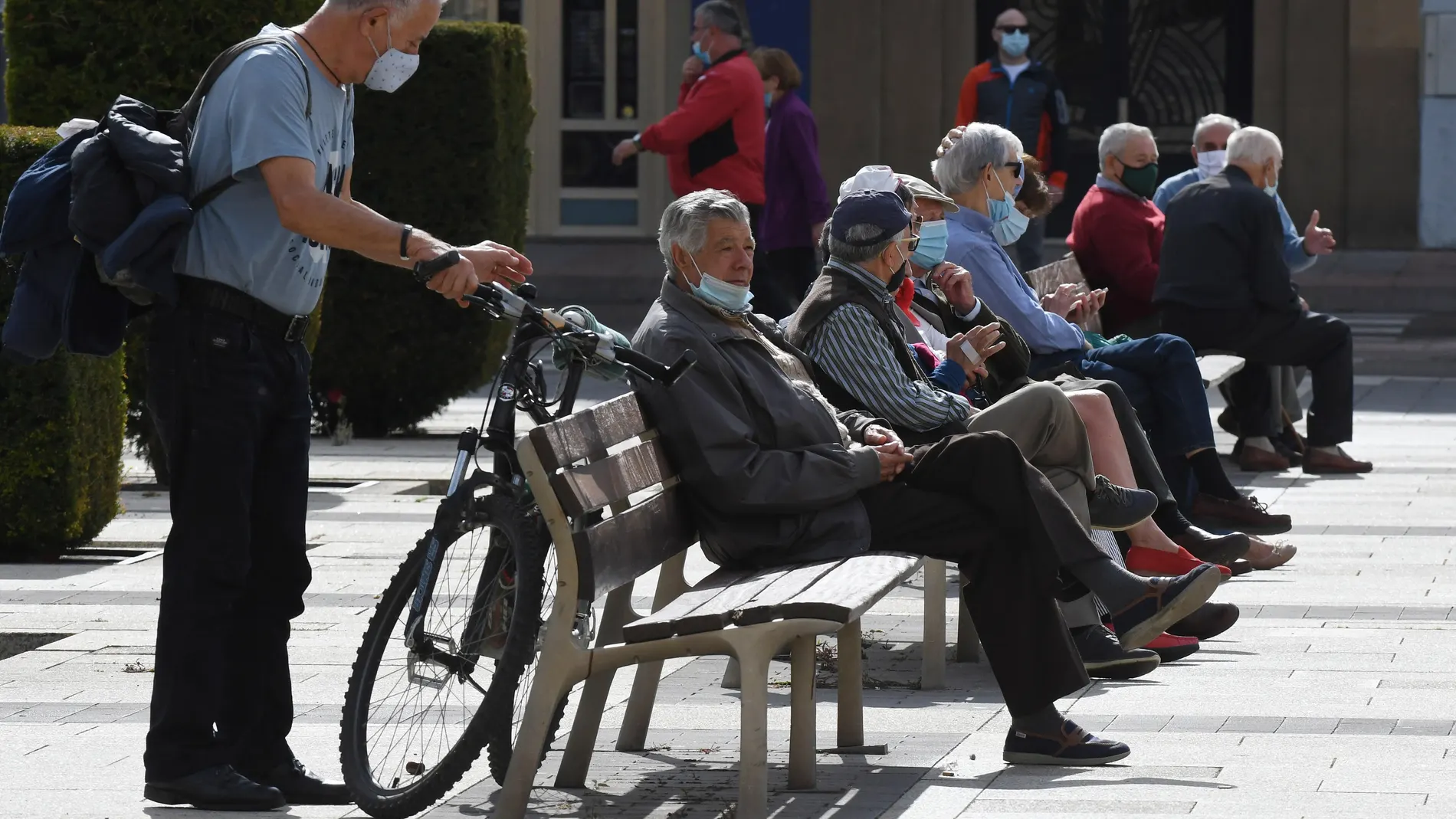 Varias personas descansan en un banco protegidos con mascarilla en León