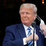 El presidente Donald Trump se quita la mascarilla al salir el sábado al balcón de la Casa Blanca