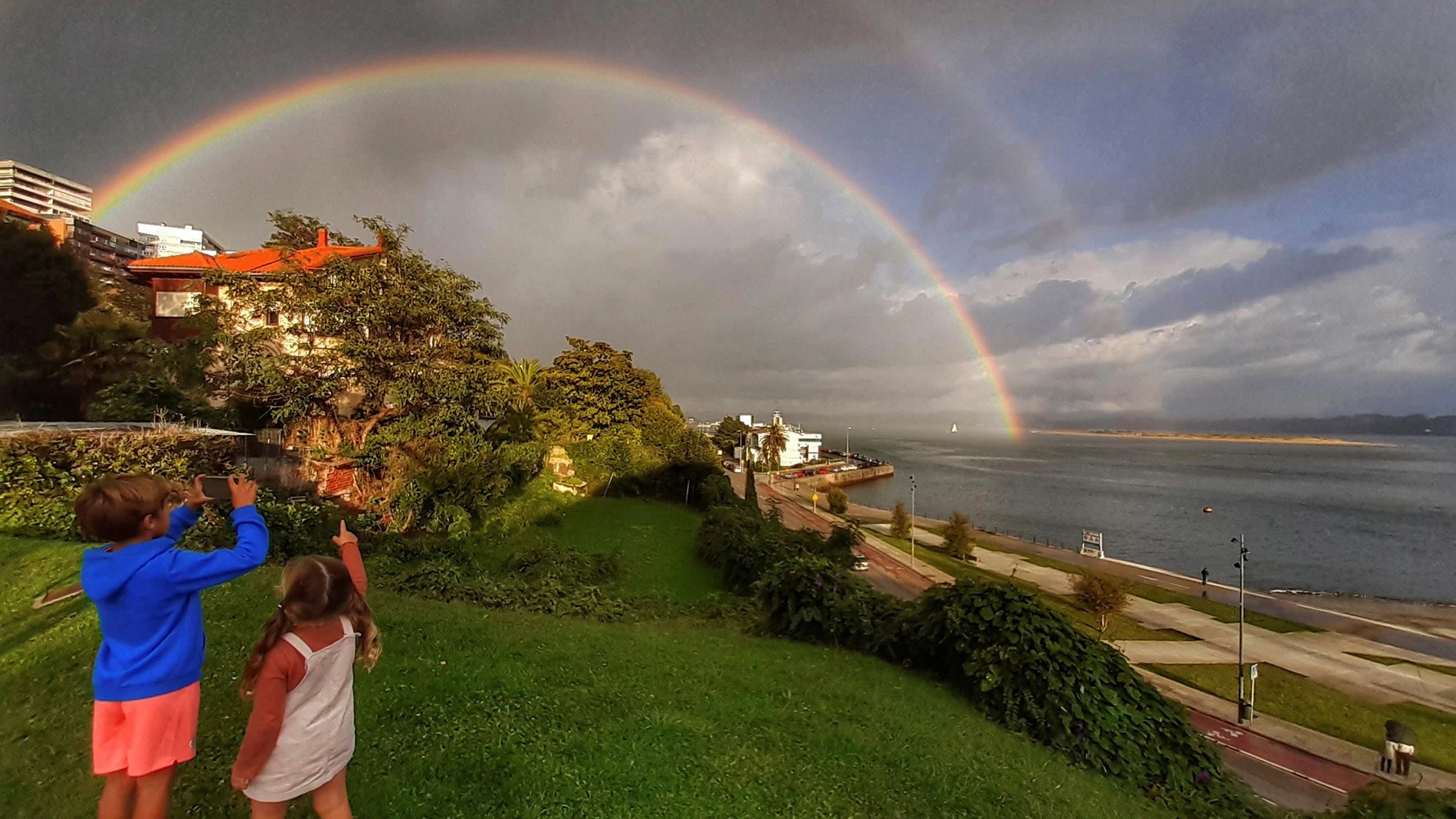 Unos niños observan el doble arco iris sobre la bahía de Santander, este jueves