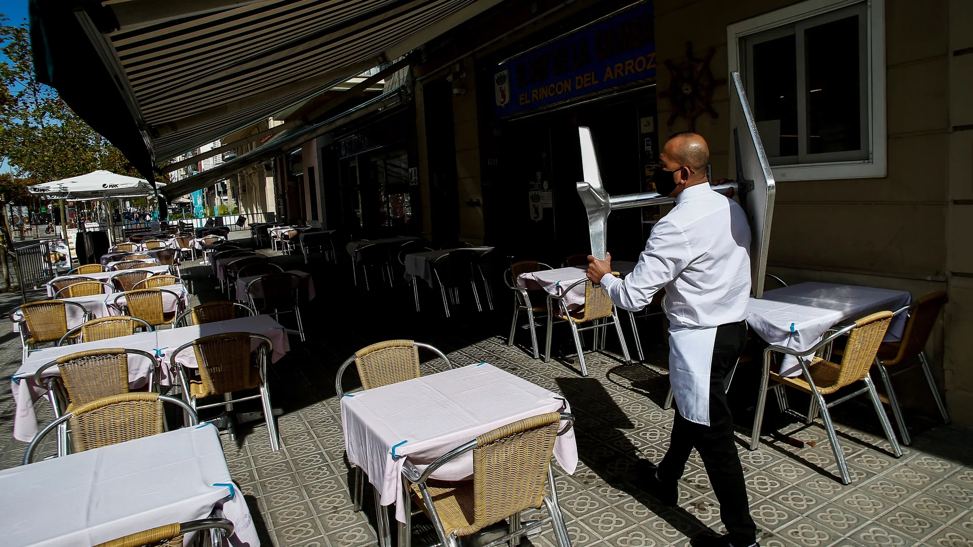 Un camarero recoge una mesa en un restaurante del barrio de la Barceloneta de Barcelona, este jueves, a la espera de que mañana entre en vigor el cierre de bares y restaurantes durante 15 días.