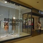 Wearing masks to curb the spread of the new coronavirus, a couple walks out of a clothing store that has a sign on a display window that reads in Spanish "Welcome back again!" at the Abasto Shopping Mall in Buenos Aires Argentina, Wednesday, Oct. 14, 2020. After seven months of closure, Buenos Aires shopping malls are reopening as the country is experiencing a spike of COVID-19 cases in the interior of the country. (AP Photo/Victor R. Caivano)