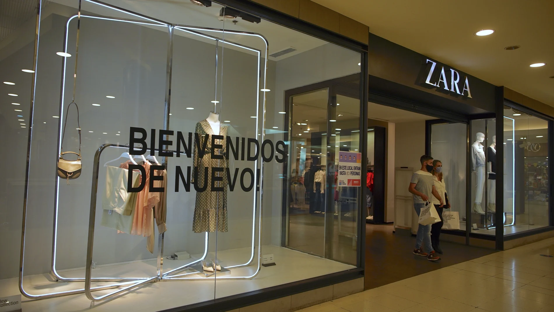 Wearing masks to curb the spread of the new coronavirus, a couple walks out of a clothing store that has a sign on a display window that reads in Spanish "Welcome back again!" at the Abasto Shopping Mall in Buenos Aires Argentina, Wednesday, Oct. 14, 2020. After seven months of closure, Buenos Aires shopping malls are reopening as the country is experiencing a spike of COVID-19 cases in the interior of the country. (AP Photo/Victor R. Caivano)