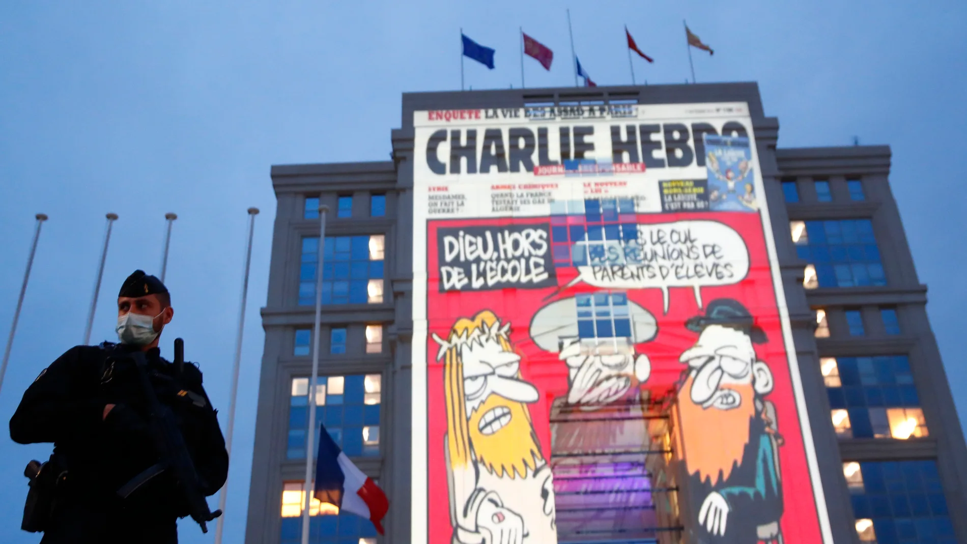 Un agente de Policía observa la proyección de caricaturas del periódico satírico francés "Charlie Hebdo" en edificios del centro de Montpellier, el año pasado