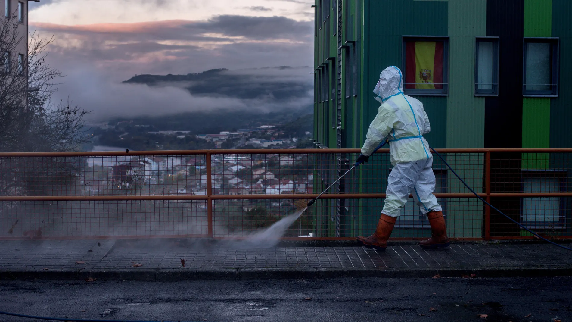 Una bandera de España cuelga de la ventana de un edificio mientras un operario municipal realiza labores de desinfección esta mañana en Orense (Galicia).