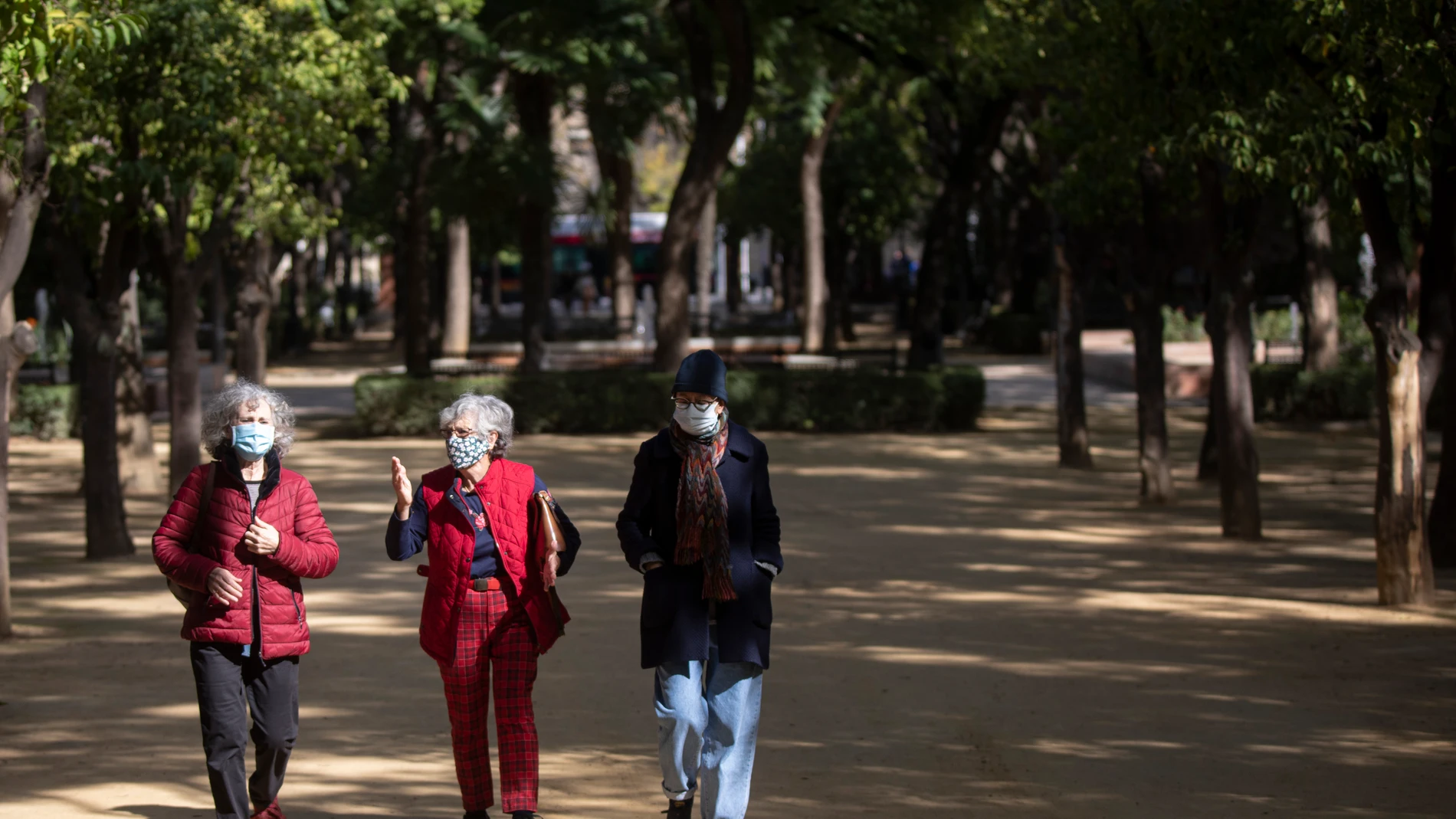 Tres personas se protegen con mascarillas mientras pasean por un parque sevillano