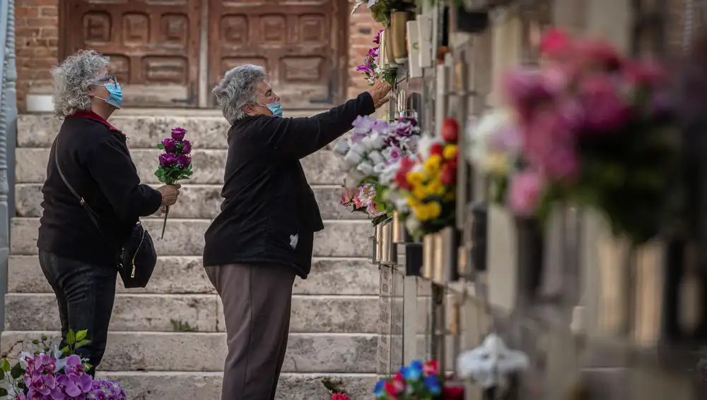 Varias mujeres colocan flores en una tumba del cementerio de Alcalá de Henares, días antes de la celebración del Día de Todos los Santos