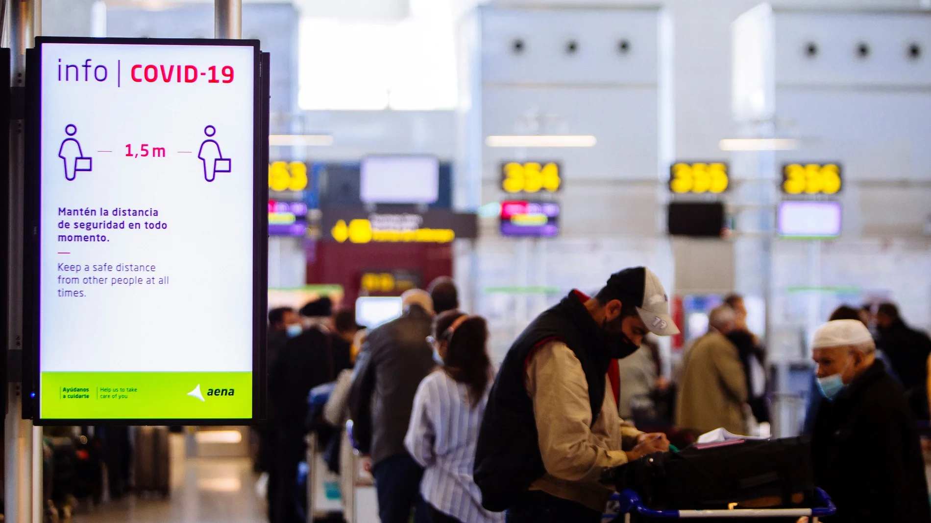 Imagen de archivo de una pantalla que informa sobre la distancia a mantener entre personas frente a una cola de embarque en el aeropuerto Costa del Sol en Málaga