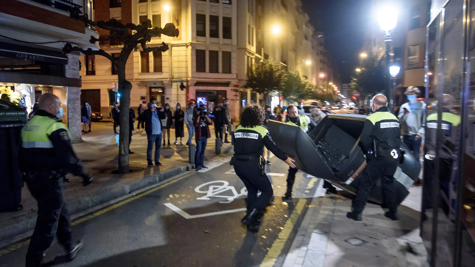 Miembros de la Policía Municipal retiran los contenedores volcados en la calzada por los participantes en las protestas en las calles de Bilbao