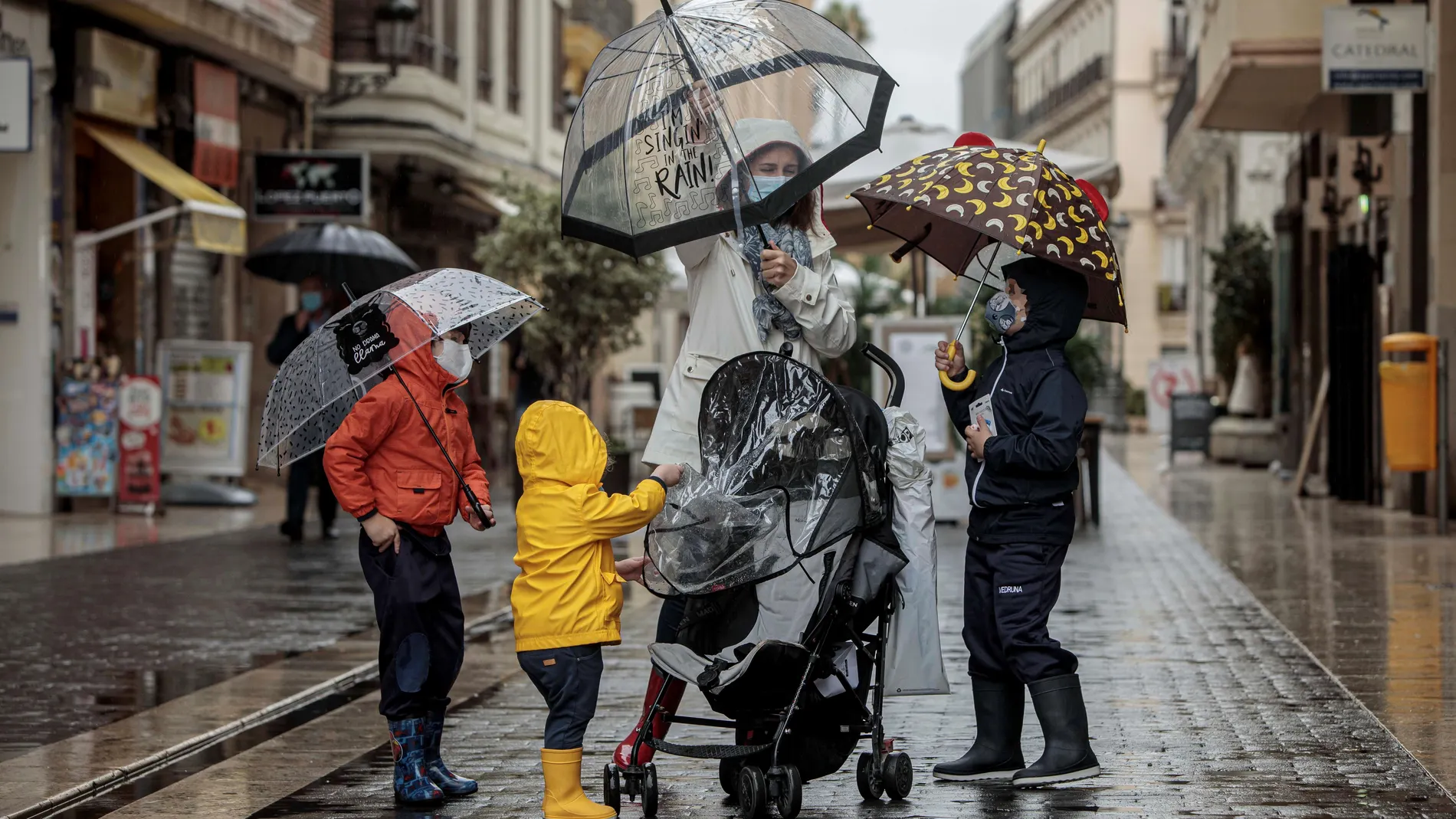VALENCIA,- Una mujer con tres menores se protegen de la lluvia con paraguas y chubasqueros en una céntrica calle de Valencia. EFE/Biel Aliño