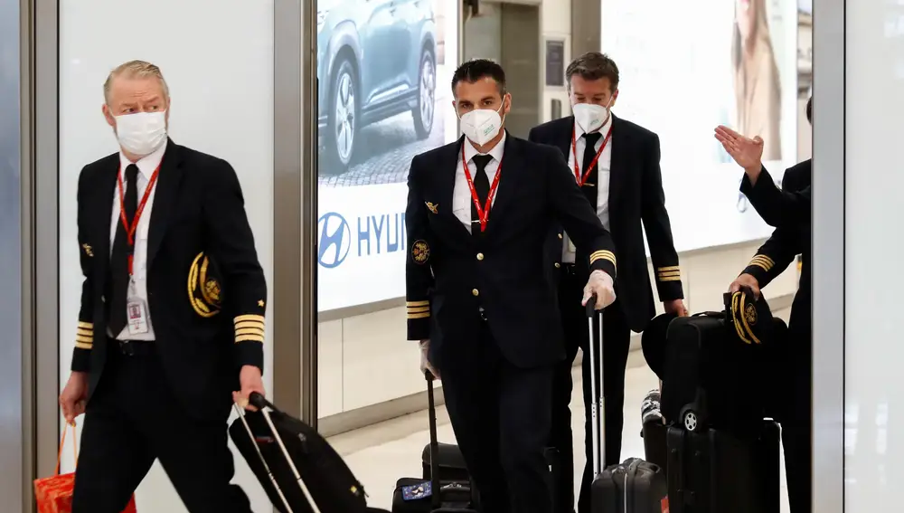 Varios pilotos y personal de vuelo protegidos con mascarilla salen del área de controles sanitarios a pasajeros en la terminal 4 del Aeropuerto de Madrid-Barajas Adolfo Suárez