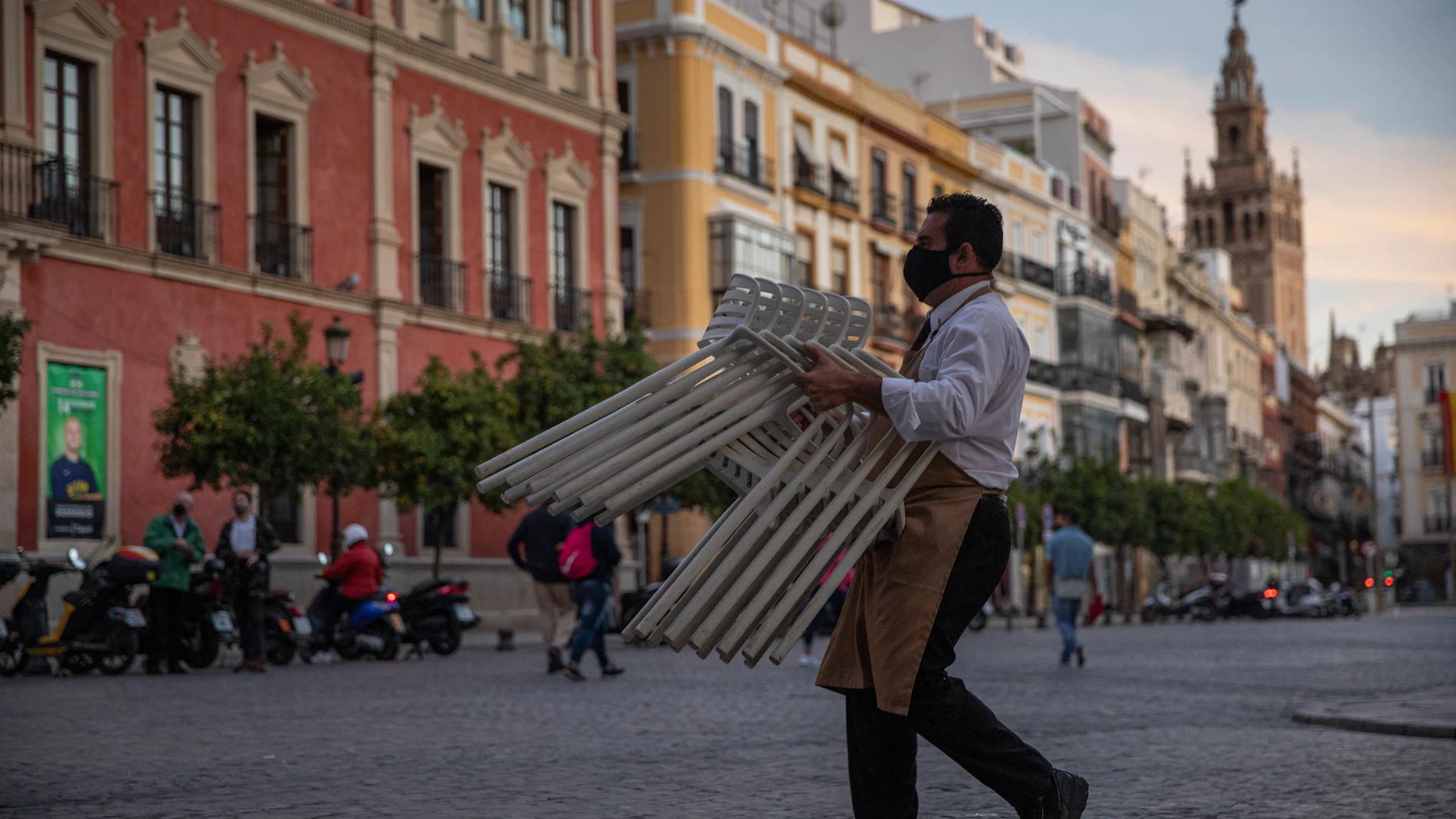 Un hostelero recoge el mobiliario de la terraza de un bar en Sevilla