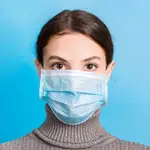 Portrait of young woman wearing medical mask at blue background. Protect your health. Coronavirus concept