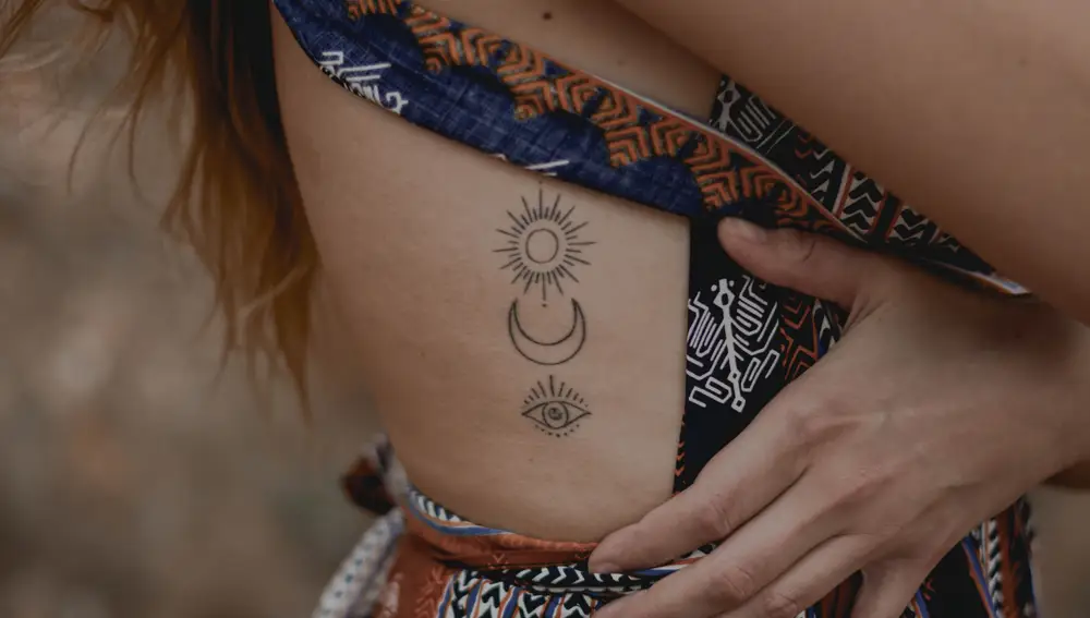 En la imagen, una mujer muestra sus tres tatuajes minimalistas.