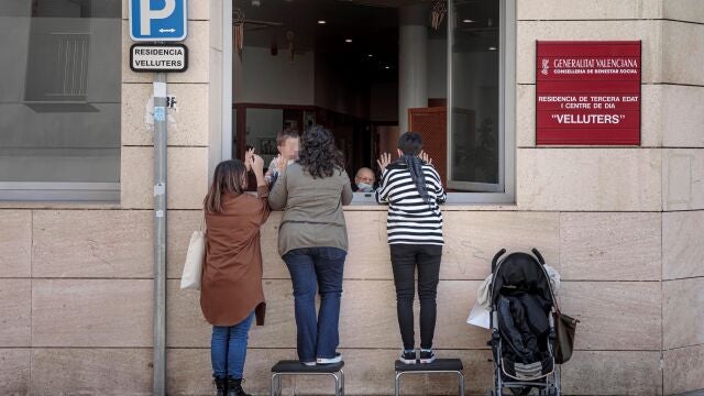 Una anciana recibe la visita de sus nietas a través de una ventana de la residencia de Velluters