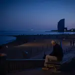 Un hombre sentado en un banco delante de la playa y el Hotel W Barcelona, en Barcelona