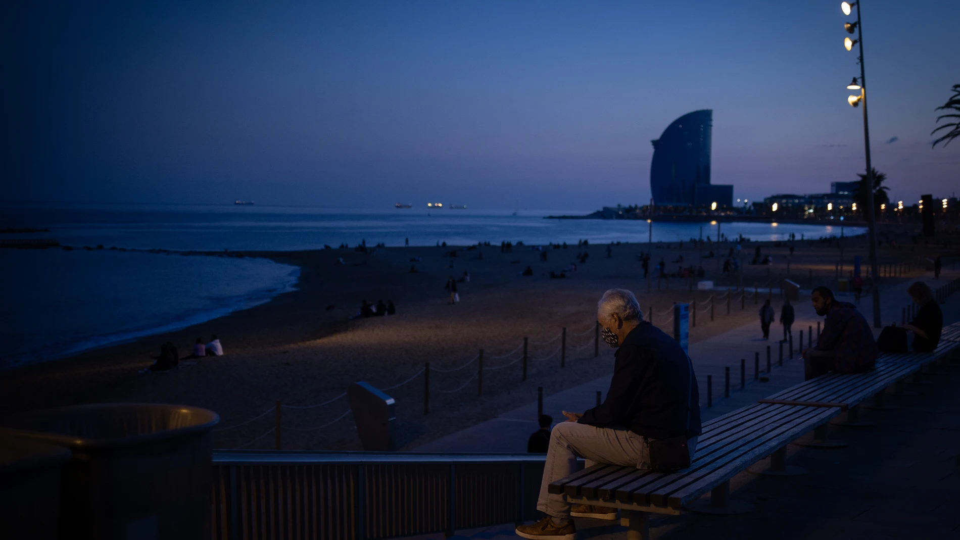 Un hombre sentado en un banco delante de la playa y el Hotel W Barcelona, en Barcelona