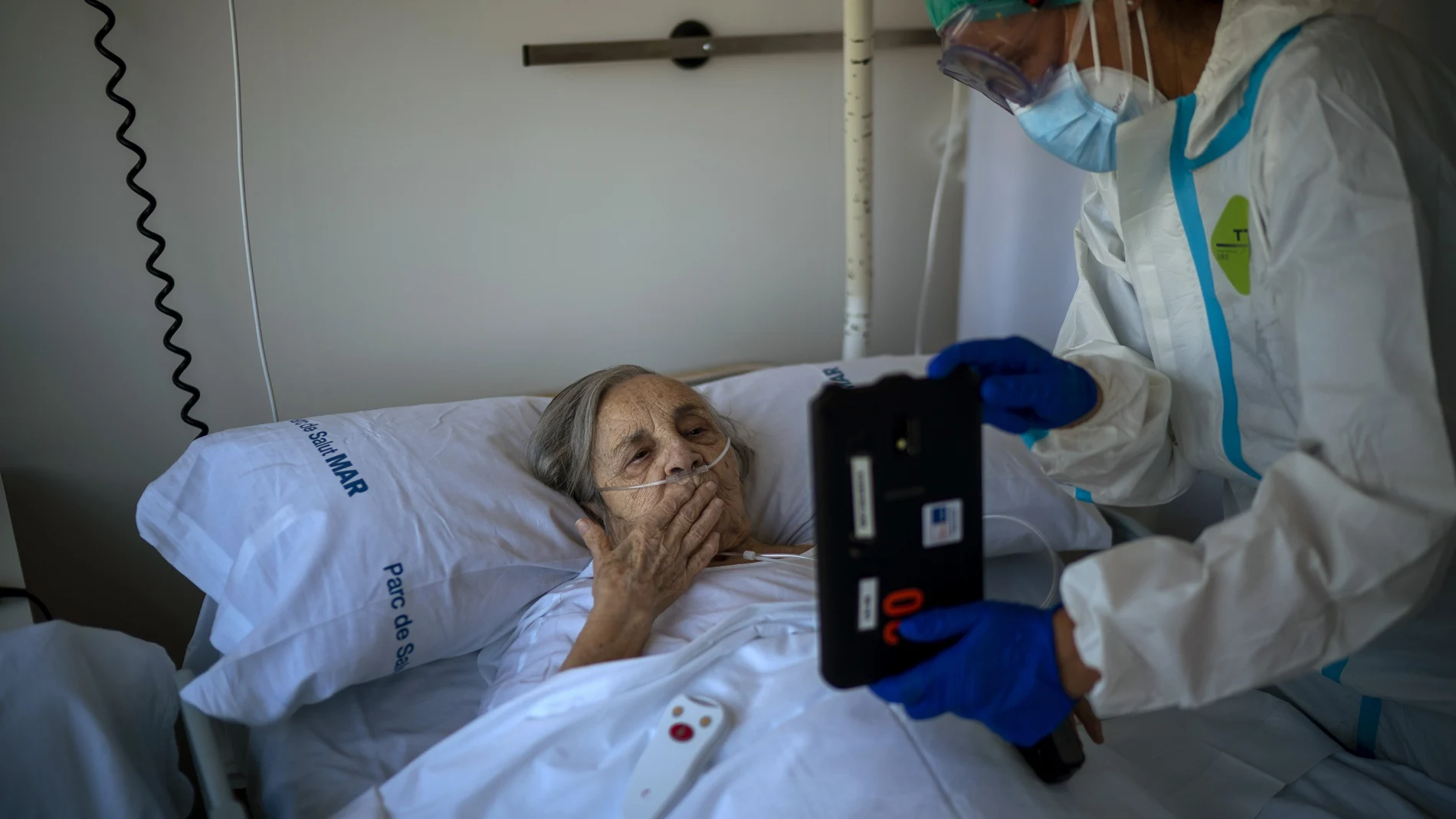 La enfermera del Hospital del Mar, Marta Fernández, sostiene una tablet para que Maria Teresa Argullos pueda hablar con su hermana. (AP Photo/Emilio Morenatti)