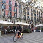 Un ciclista pasa junto a varias terrazas de Las Ramblas de Barcelona, que hoy permanecen cerradas en la víspera de su apertura
