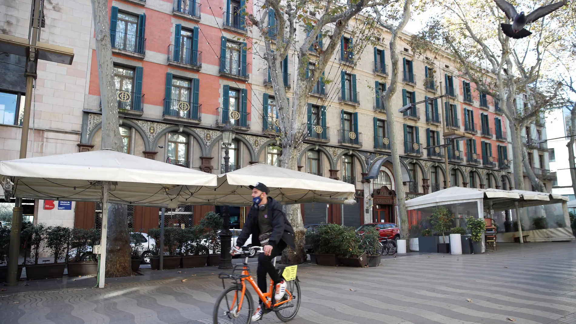 Un ciclista pasa junto a varias terrazas de Las Ramblas de Barcelona, que hoy permanecen cerradas en la víspera de su apertura