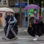 Dos jóvenes se protegen de la lluvia con paraguas en la Avenida Gerónimo de Roda, Murcia