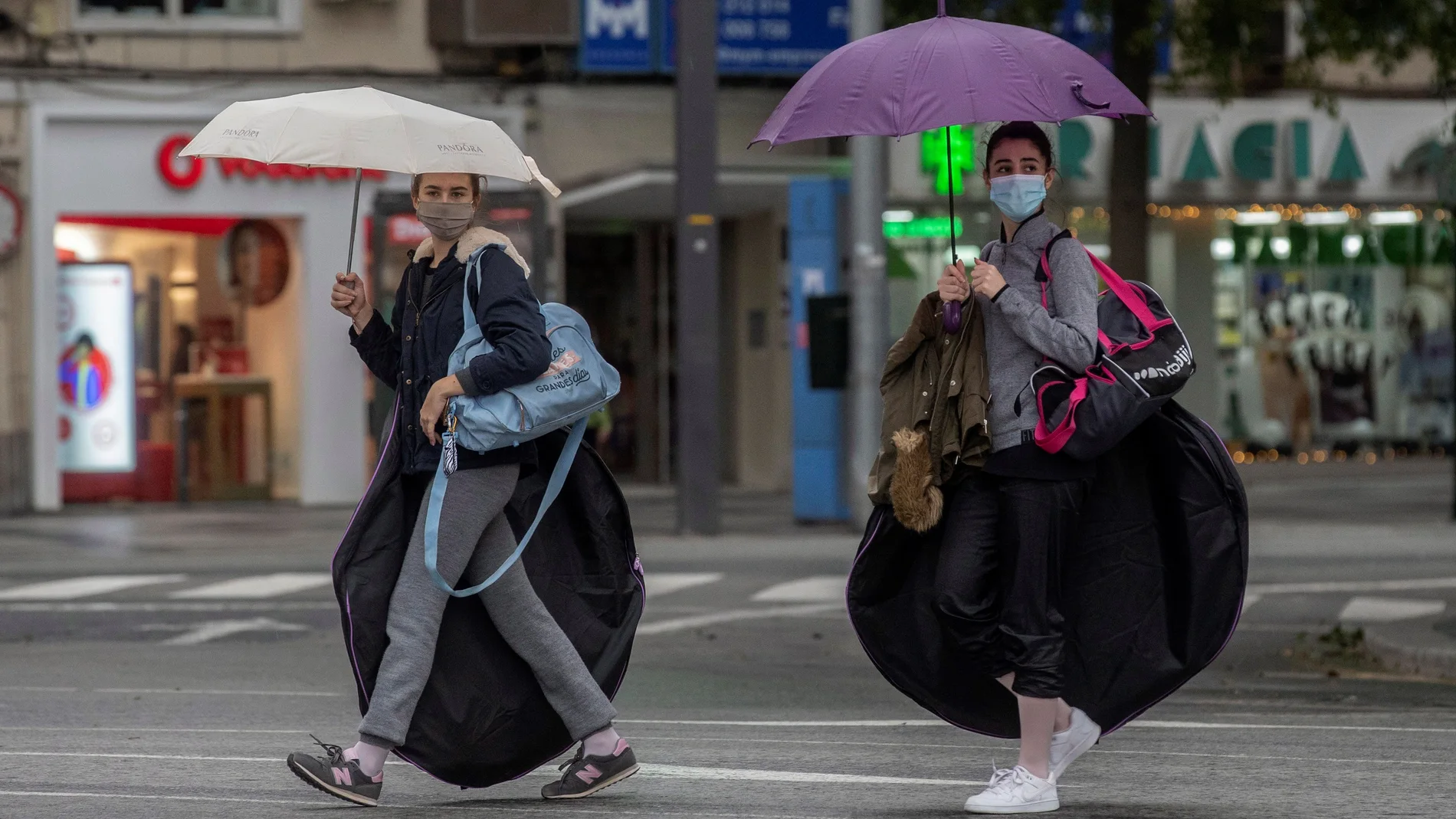 Dos jóvenes se protegen de la lluvia con paraguas en la Avenida Gerónimo de Roda, Murcia