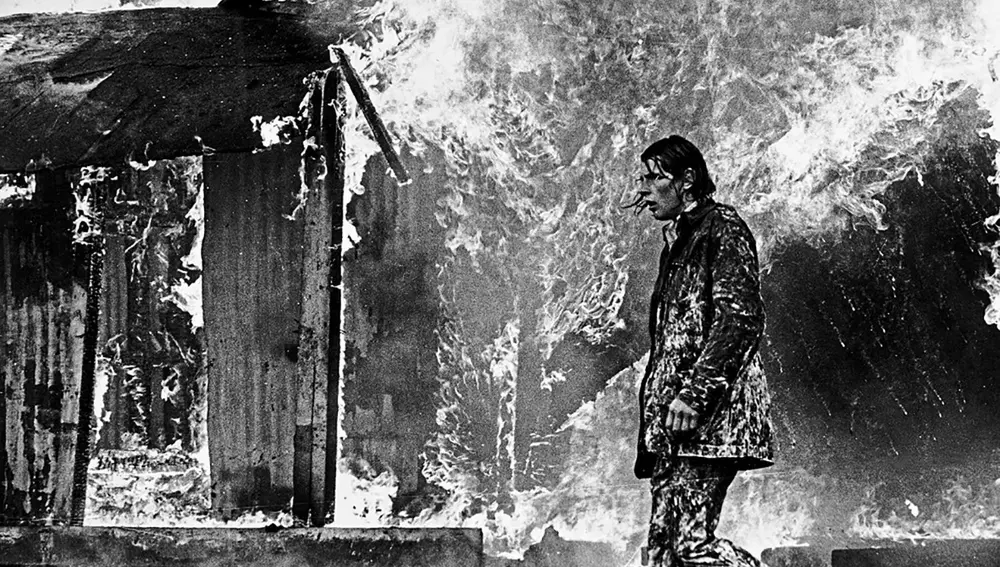 Un hombre camina ante un edificio ardiendo durante los disturbios de los Troubles de Irlanda