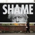Un hombre pasea en una calle de Manchester junto a un cartel crítico con la gestión de Boris Johnson del coronavirus donde se puede leer «Vergüenza»