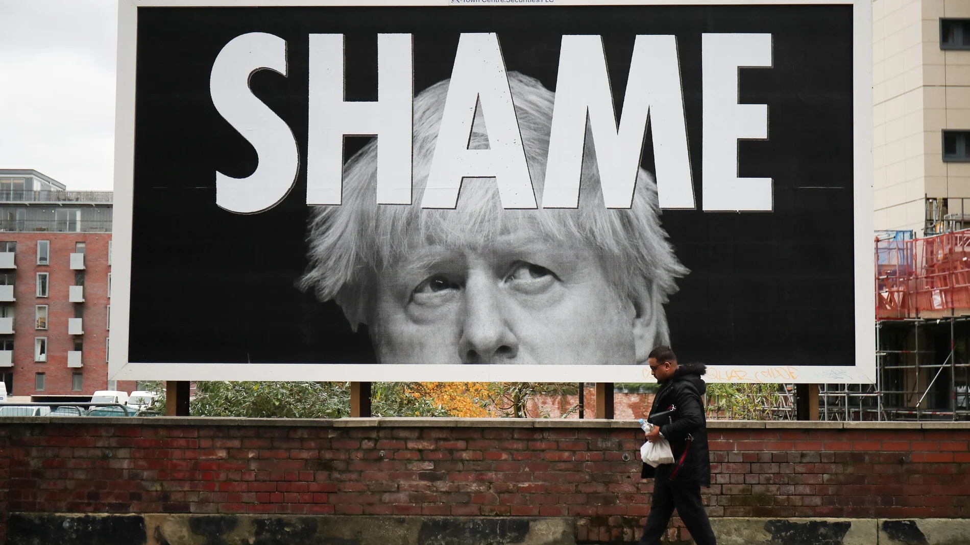 Un hombre pasea en una calle de Manchester junto a un cartel crítico con la gestión de Boris Johnson del coronavirus donde se puede leer «Vergüenza»